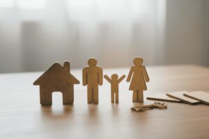 Wooden family figures beside a model house and keys on a desk, representing separation, parenting and property matters